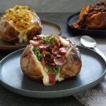 Três batatas recheadas A Batata Que Voa em pratos escuros: frente com brócolis bacon e catupiry, ao fundo frango desfiado e picanha ao molho de cerveja