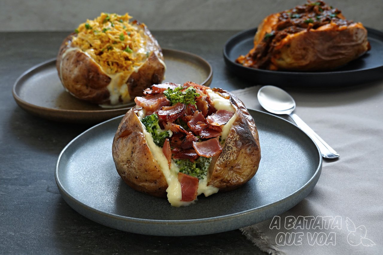 Três batatas recheadas A Batata Que Voa em pratos escuros: frente com brócolis bacon e catupiry, ao fundo frango desfiado e picanha ao molho de cerveja