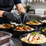 Cardápio para dark kitchen com bowls de frango, massas e embalagens de delivery em cozinha moderna iluminada
