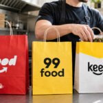Restaurante prepara pedidos para delivery com sacolas do iFood, 99Food e Keeta sobre balcão de cozinha profissional